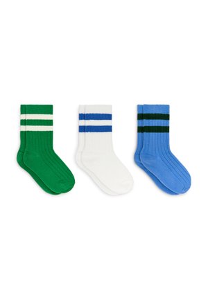 Trois paires de chaussettes côtelées montantes vertes avec des rayures blanches, blanches avec des rayures bleues, et bleues avec des rayures vert foncé, posées à plat côte à côte.