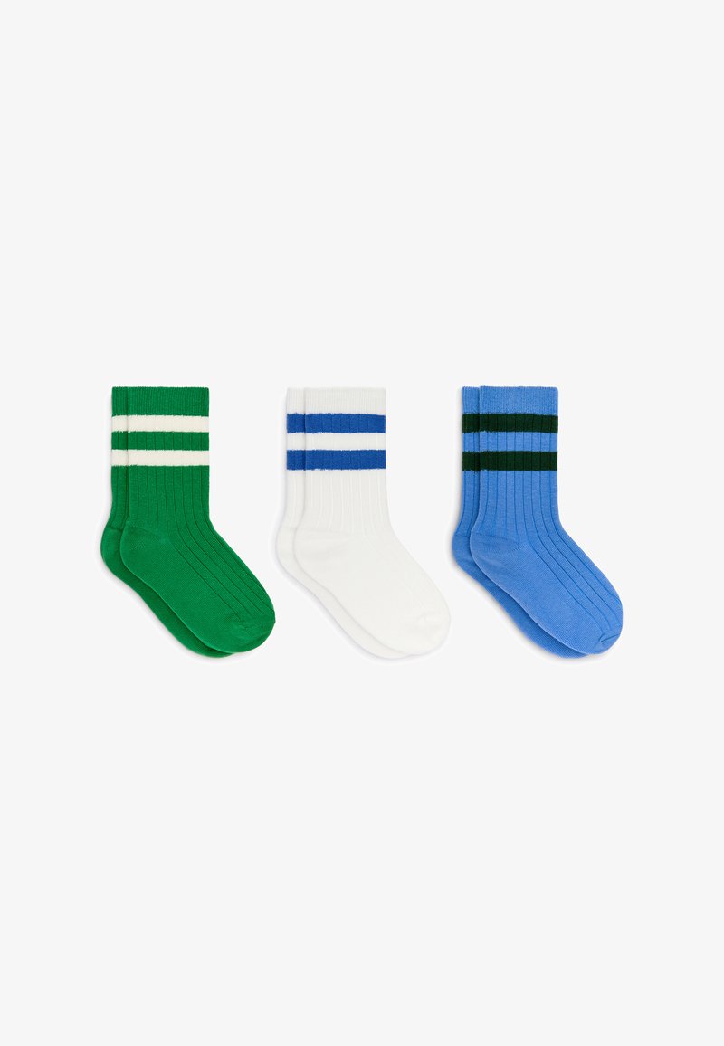 Trois paires de chaussettes côtelées montantes vertes avec des rayures blanches, blanches avec des rayures bleues, et bleues avec des rayures vert foncé, posées à plat côte à côte.