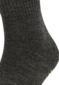 Mørkegrå sokk laget av et strukturert strikket stoff, med forsterket hælområde og en liten lysegrønn detalj nær ankelen.