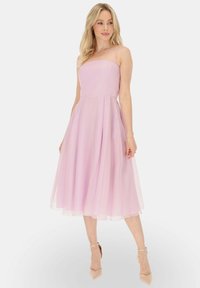 Jasnoróżowa midi sukienka z dopasowanym topem, ramiączkami w stylu spaghetti oraz zwiewnym, warstwowym tiulowym dołem, w zestawieniu z cielistymi szpilkami.