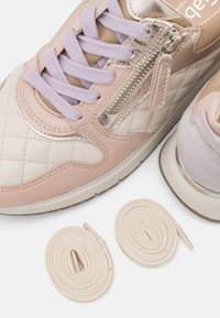 Sneakers with a quilted light pink leather upper, metallic accents, lavender laces, and two rolled beige laces beside them.