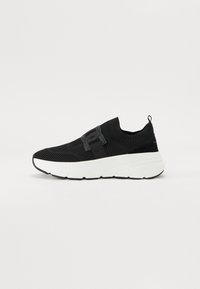 Baskets noires de sport avec une tige en tricot, dotées d'une sangle bien visible. Semelle épaisse blanche avec une finition texturée et des accents noirs.