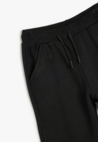 Los pantalones de chándal negros cuentan con una cintura acanalada con un cordón ajustable y bolsillos laterales, fabricados con una tela suave y texturizada.