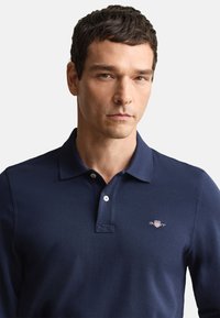 Tmavomodré polokošeľa z textúrovaného bavlneného materiálu s troma gombíkmi na golieri a malým vyšívaným logom na hrudi.