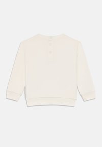 Sweatshirt couleur crème avec un col rond, trois boutons à l'arrière et des manches longues. Fabriqué en tissu doux avec des poignets côtelés.