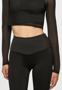 Czarny krótki top z długim rękawem o prążkowanej fakturze, zestawiony z czarnymi legginsami o wysokim stanie z gładkim wykończeniem i warstwowym pasem.