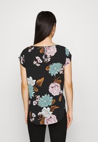 Blouse noire à motif floral, dotée de manches courtes, d'un col rond et d'une fermeture en forme de clé au dos. Le tissu présente de grandes fleurs pastel et des feuilles.