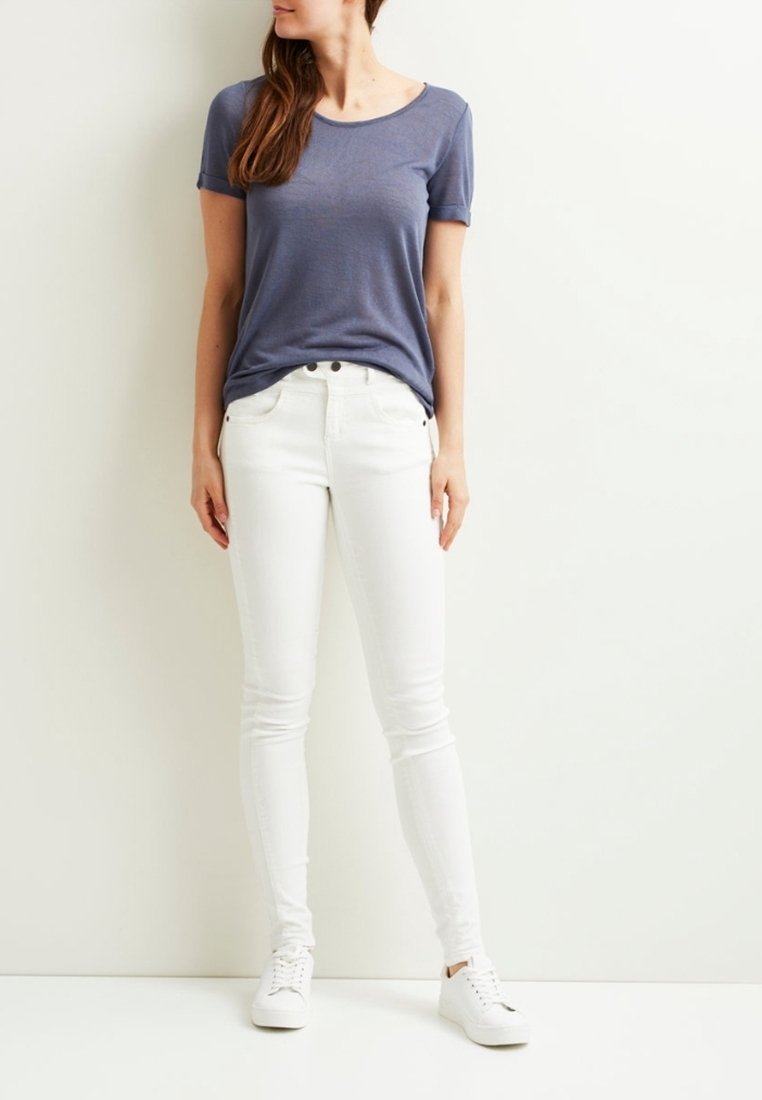 Chemise bleue à manches courtes associée à un jean skinny blanc et à des baskets blanches, mettant en avant un design décontracté avec une texture lisse.