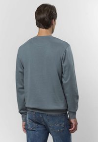 Szara bluza z okrągłym dekoltem, ściągaczami na rękawach i u dołu. Gładka faktura, prosty design. Noszona z niebieskimi jeansami.