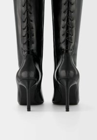 Svarta läderstövlar med hög klack och en elegant design, med en bakre snörning och spetsig tå. Texturerad yta med dragkedjestängning.