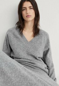 Maglione grigio a V realizzato in morbido materiale texturizzato con dettagli a coste sul colletto. Vestibilità rilassata e maniche lunghe.