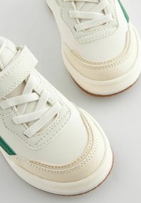 Hvide lædersneakers med grønne detaljer, der har snørebåndslukning, gummisål og struktureret syning langs siderne og tåen.