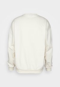 Sudadera de color crema con escote redondeado, hombros caídos y puños acanalados. Textura suave y ajuste relajado sin gráficos visibles.