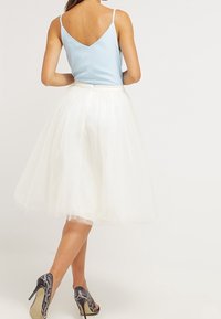 Top sin mangas de color azul claro con escote en V, acompañado de una falda de tul blanca hasta la rodilla. Presenta tacones de estampado de serpiente gris.