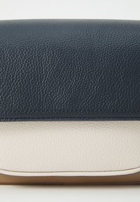 Textured leather clutch in navy blue and cream, featuring a smooth finish and stitched detailing along the seams. Rectangular shape, slim profile.