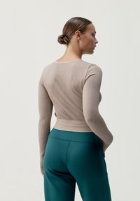 Bežový rebrovaný dlhý rukáv top s obtiahnutým strihom, okrúhlym výstrihom a textúrovanými detailmi, kombinovaný s petrolejovými legínami s vysokým pásom.