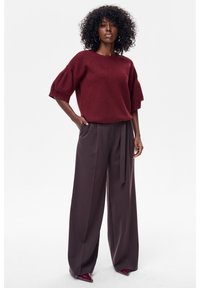 Bordowy sweter na drutach z bufkami, zestawiony z ciemnymi, szerokimi spodniami z wysokim stanem. Strój uzupełnia przewiązany pasek i eleganckie buty.