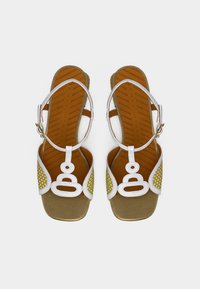 Sandales blanches et jaunes avec un accent doré. Présentent un design géométrique et une texture perforée sur les côtés. Comprennent une bride réglable à la cheville.