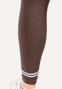 Leggings de sport marron à texture lisse, avec des doubles rayures blanches à l'ourlet. Conçus pour un ajustement près du corps, adaptés aux vêtements de sport.