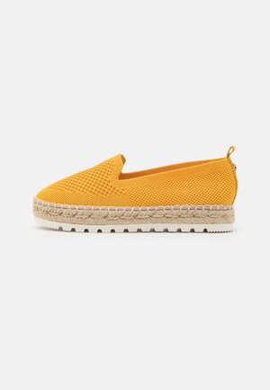 Chaussure jaune tissée sans lacets avec une tige texturée, une semelle en corde d'espadrille beige et une semelle inférieure en caoutchouc blanc. Tirette arrière pour un enfilage facile.