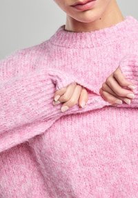 Pink knitted sweater with a round neckline and ribbed cuffs. The texture is soft and fuzzy, featuring a blend of light and darker pink hues.
