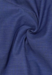 Granatowa tkanina z teksturowanym wzorem drobnych białych kropek, charakteryzująca się gładkim wyglądem i lekkim układem.