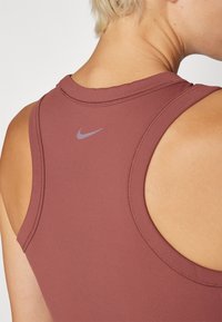 Maroon athletic tank top with a high neckline, smooth texture, and reinforced stitching. Features a small gray Nike logo on the back.