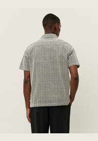 Chemise à manches courtes avec un motif noir et blanc en tourbillons, fabriquée dans un tissu léger, dotée d'un col et d'une coupe décontractée.