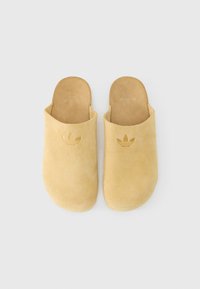 Suede slip-on clogs in light yellow, featuring a rounded toe and an embossed logo on the upper. Smooth interior lining and seamless design.