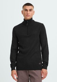 Black zip-neck sweater featuring long sleeves, ribbed cuffs, and hem. Soft texture with a small logo patch on the lower side.