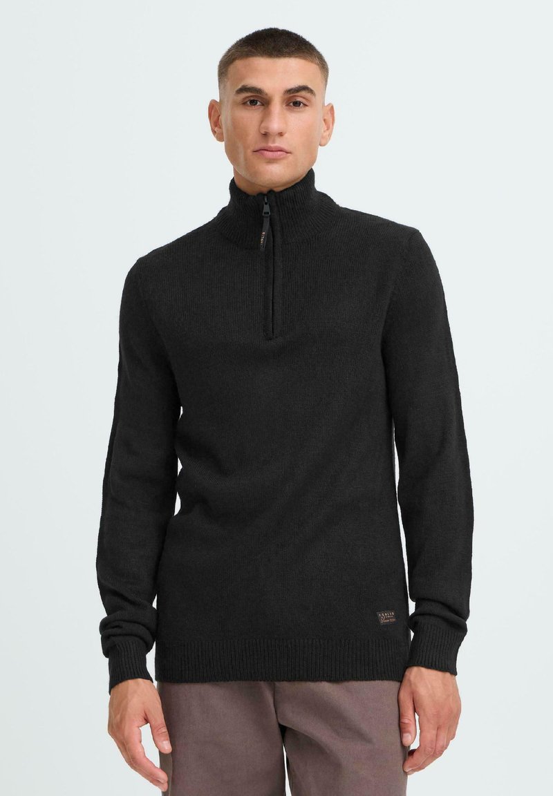 Black zip-neck sweater featuring long sleeves, ribbed cuffs, and hem. Soft texture with a small logo patch on the lower side.