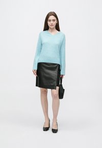 Svetlo modra pulover z v-izrezom, mehka tekstura, kombinirana s črno usnjeno svinčnikasto krilo s stranskim razporkom in črnimi čevlji z visokimi petami.