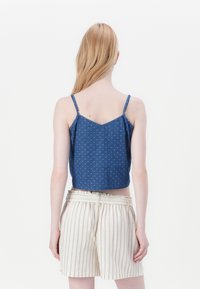 Top scurt din bumbac de culoare bleu închis, cu bretele, având un mic model cu buline; asortat cu pantaloni scurți ușor rayurați, cu talie elastică.