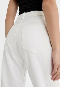 Pantaloni bianchi in cotone con un tessuto testurizzato, dotati di due tasche posteriori e un'etichetta che mostra il nome del marchio. Design a gamba dritta.