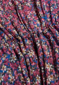 Tissu floral présentant des fleurs roses et blanches sur un fond bleu, avec une texture plissée et un matériau léger.