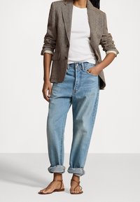 Brun herringbone-blazer över en vit t-shirt, i kombination med ljusblå uppvikta jeans och bruna sandaler med remmar. Enkelt, avslappnat outfit.