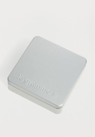 Petite boîte métallique carrée argentée avec des coins arrondis et le texte embossé "le gramme" sur le couvercle.