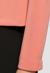 Helles rosa Langarmoberteil mit abgerundetem Saum, ausgestattet mit einer weichen Textur und cuffs, kombiniert mit einem schwarzen Unterteil.