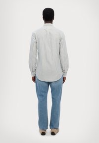 Camicetta a righe blu chiaro con maniche lunghe, polsini abbottonati e orlo curvo, abbinata a pantaloni in denim chiaro e calzature beige.