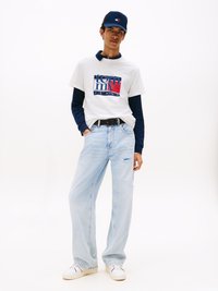 Witte T-shirt met een blauw en rood "Tommy Jeans" graphic, gelaagd over een marineblauw longsleeve shirt. Lichtblauwe distressed jeans en witte sneakers.