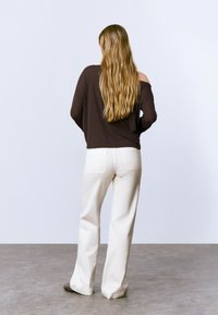 Top marrón de manga larga, de corte holgado con hombros caídos. Pantalones de pierna ancha de color claro con bolsillos traseros. Textura recta y diseño minimalista.
