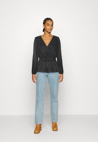 Top preto brilhante, com mangas longas e decote em V; combinado com jeans de perna reta azul claro e botins de salto castanhos.