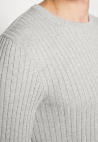 Maglione in maglia costina grigio chiaro con scollo rotondo e tessuto texturizzato. Dettaglio sui motivi a costine orizzontali e verticali lungo il corpo.