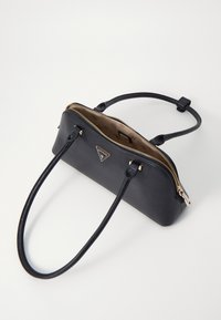 Bolsa de mão em couro preto com duas alças, fecho dourado e detalhe de logotipo. Textura lisa e forma estruturada, apresentando um topo aberto.