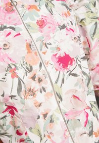 Blommig zip-tröja med vit bakgrund och rosa, gröna och orange blomstertryck; slät tyg och silver dragkedjedetalj.