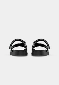 Black open-toe sandals with two adjustable straps, flat sole, matte finish, and simple design, showcasing textile and rubber materials.