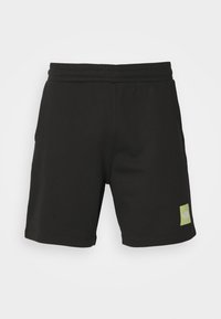 Pantalones cortos deportivos negros de tela suave con cinturilla elástica, que cuentan con bolsillos laterales y un pequeño parche de logo verde en la parte izquierda.