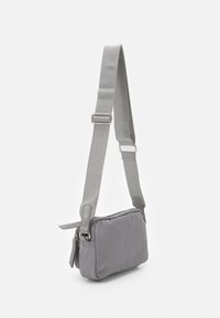 Grå crossbody-taske i stof med en glat tekstur, rektangulær form, justerbar rem og lynlåslukning. Enkel design med minimale detaljer.
