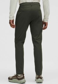 Maslinasto zelene, uske hlače napravljene od glatkog materijala, s dva stražnja džepa i kombinirane s smeškastim patikama s uzorkom.