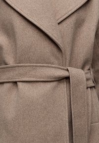 Gros plan d'un manteau en laine beige avec un large col à revers et une ceinture en tissu nouée à la taille.